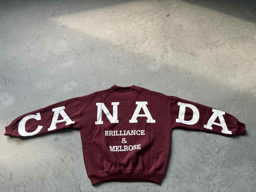 Maroon sweatshirt with 'CANADA' and text on a concrete floor